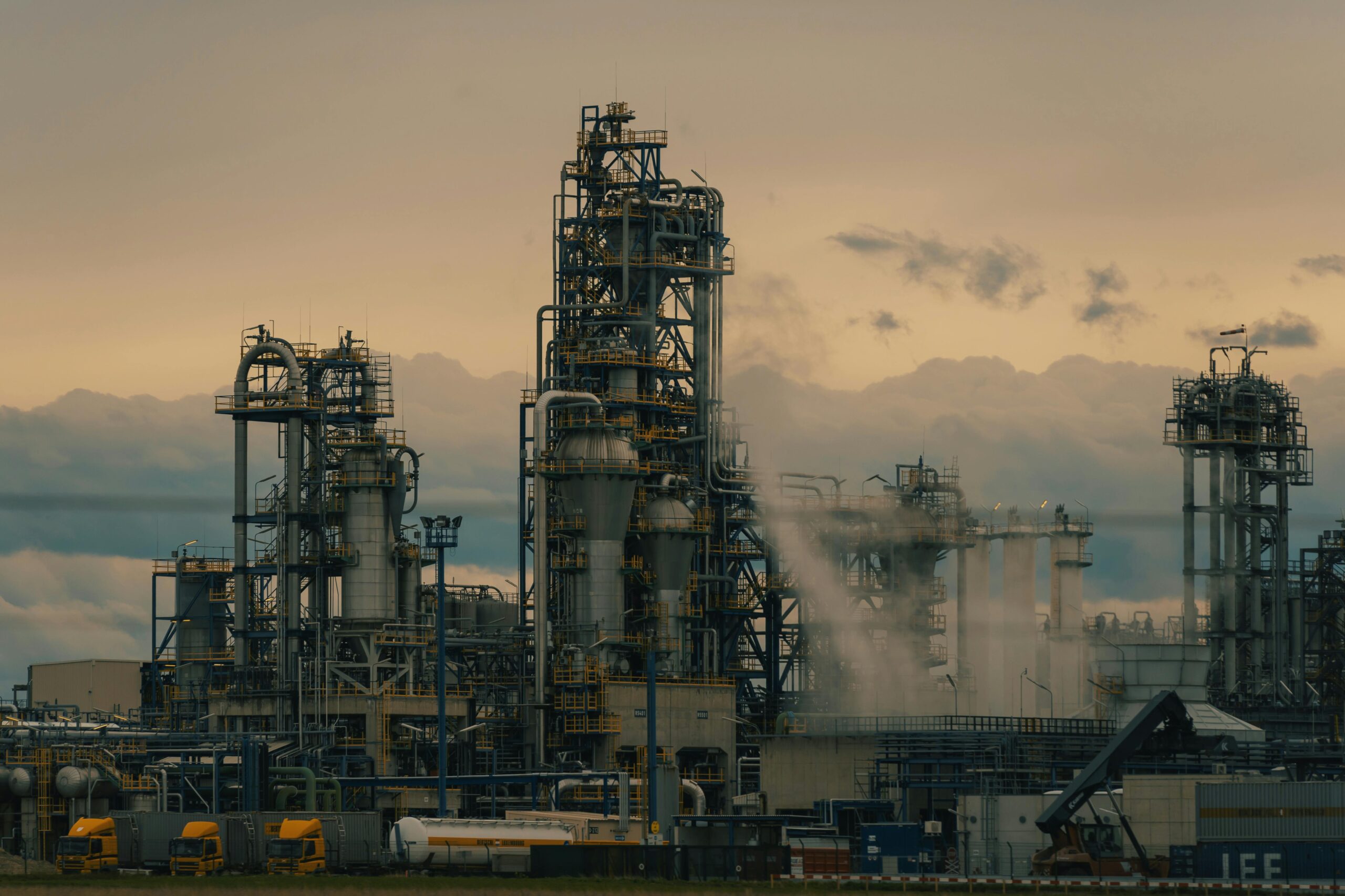 Inicio A detailed view of a refinery's towers against a cloudy dusk sky, showcasing industrial architecture.